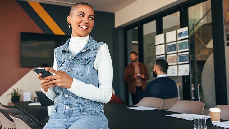 Businesswoman in an office using a smartphone and smiling.